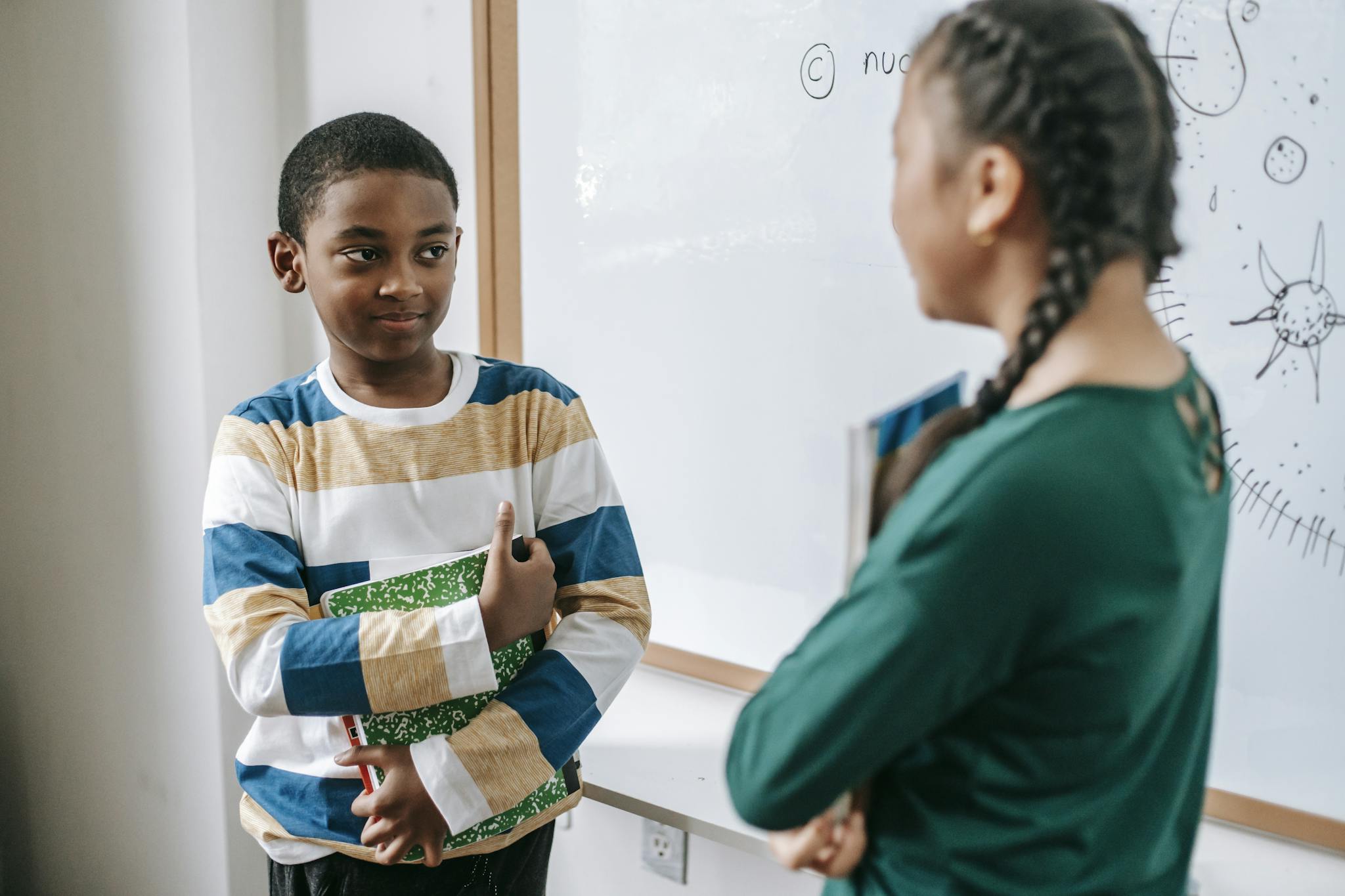 Diverse little classmates speaking near whiteboard during lesson at school